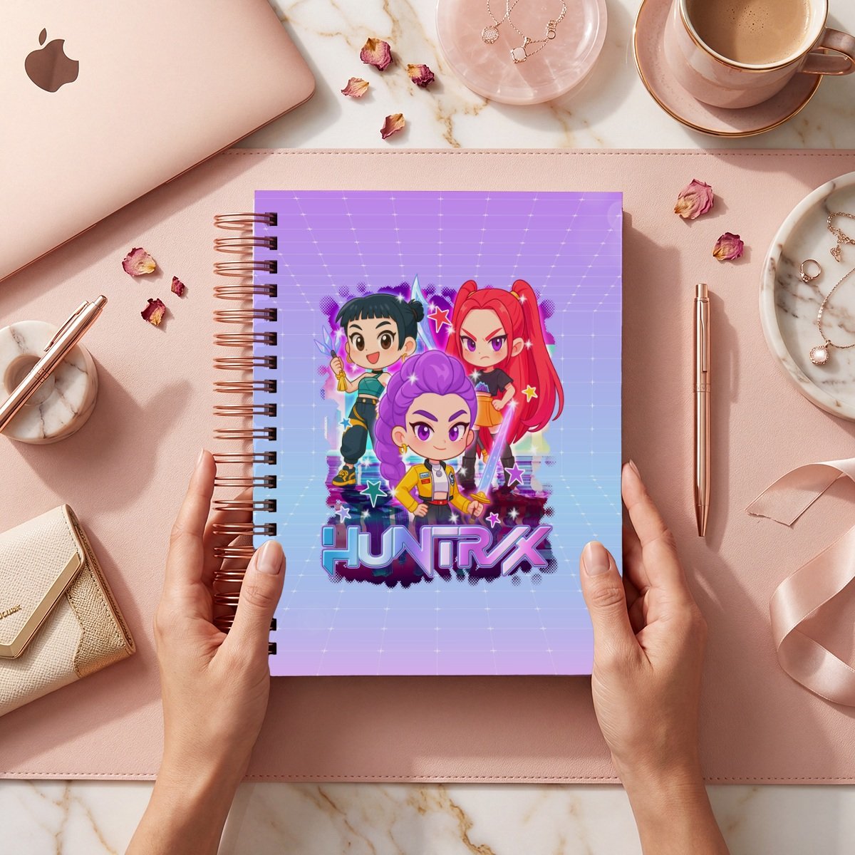 Mockup de portada Huntrix E2627-001: tres figuras y nombre Huntrix sobre retícula lila y celeste; se muestra el frente sostenido por manos, sin año impreso.